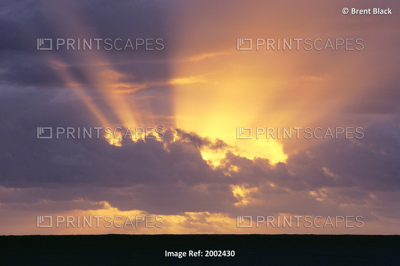 Sunrays Stream Out From Behind Clouds At Sunset, Over Dark Ocean