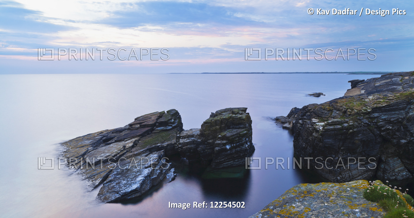 Rock And Tranquil Water Along The Coastline At Dawn; Orkney, Scotland