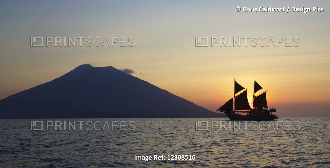 Ocean View With Yacht With Sails And Volcano Silhouetted Against The Setting Sun