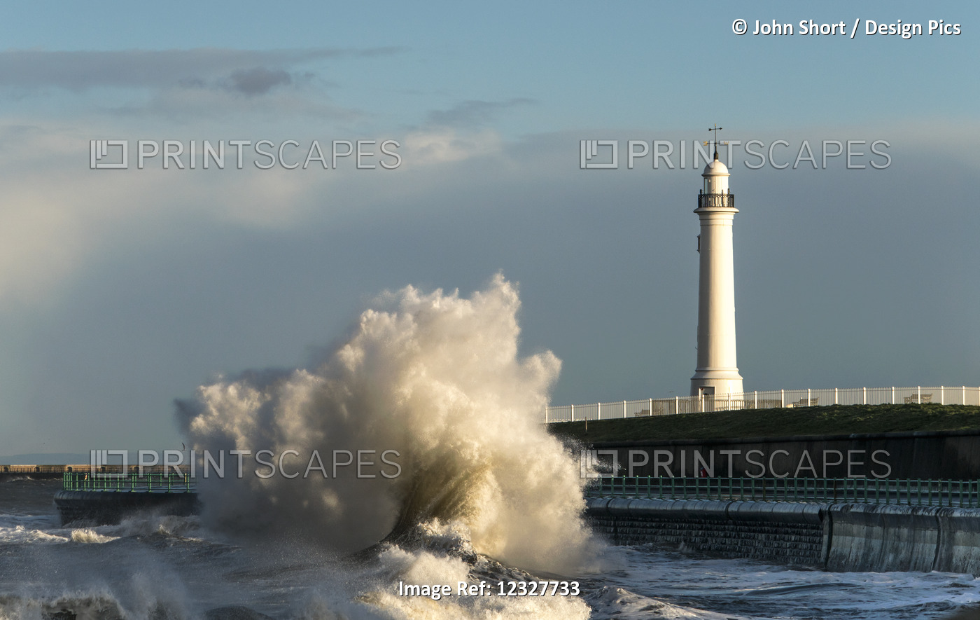 A Large Wave Crashing Against The Wall On The Shoreline Below A Lighthouse; ...