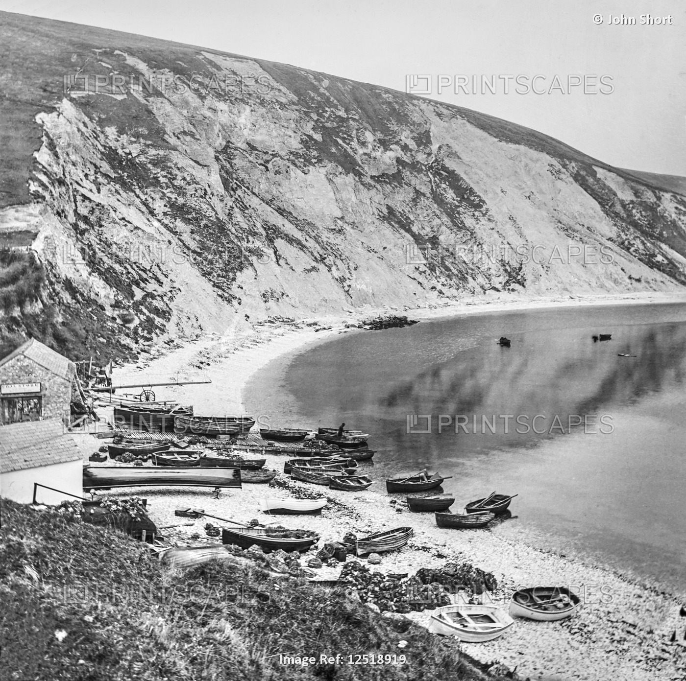 Fishing village on Lulworth Cove with boats on the shore and cliffs along the ...